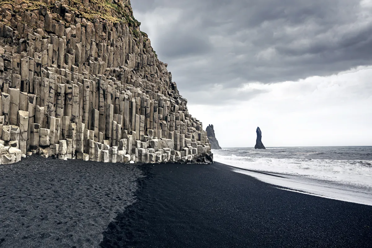 Vue panoramique des superbes plages de sable noir d'Islande, contrastant avec les vagues spectaculaires et les falaises c&ocirc;ti&egrave;res accident&eacute;es