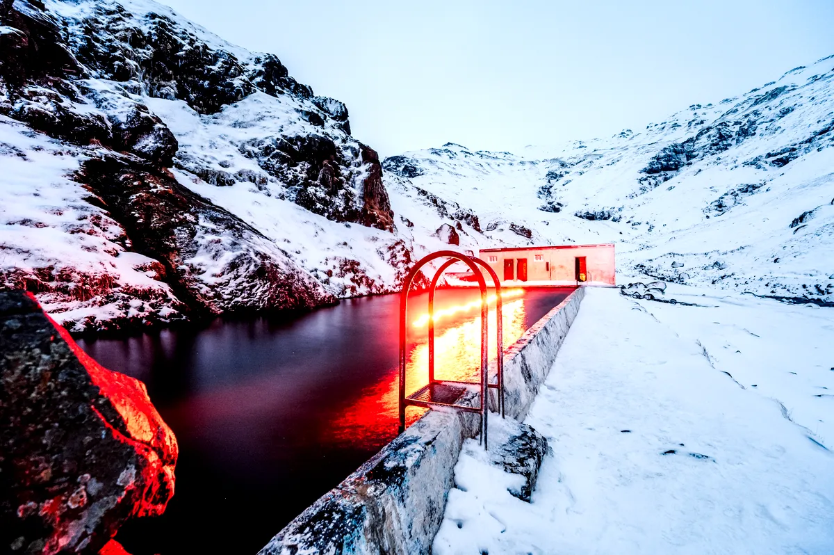 Seljavallalaug Hot Spring : Tranquillité hivernale Une piscine géothermique sereine nichée entre les pentes enneigées des montagnes à Seljavallalaug, en Islande. L'éclairage tamisé donne à la scène une lueur mystique, se reflétant sur les rochers recouverts de neige.
