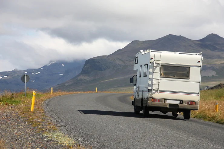 Un van aménagé roulant sur une route pittoresque en Islande, entouré de montagnes et de paysages spectaculaires—illustrant la liberté et l'aventure du voyage en van sur l'île.