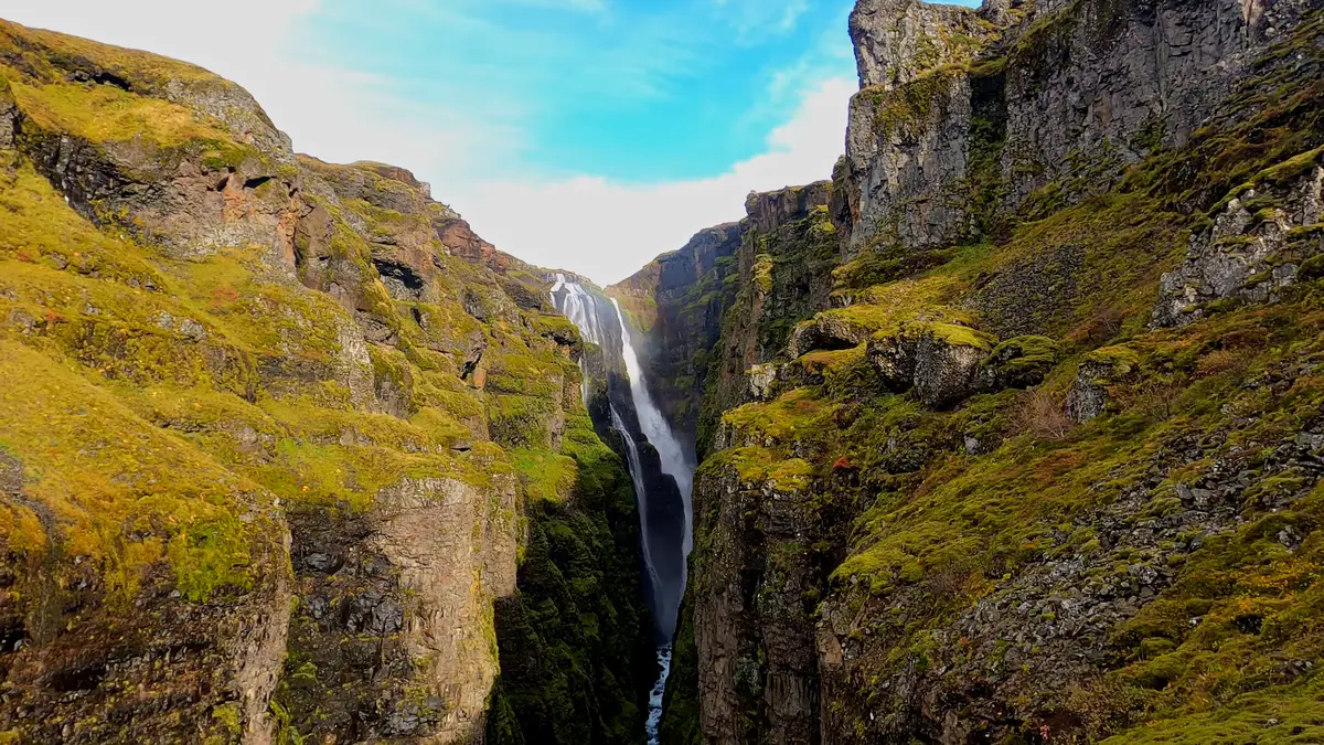 Une majestueuse cascade en Islande tombant entre d’imposantes falaises couvertes de mousse. Un lieu parfait à explorer en camping-car.