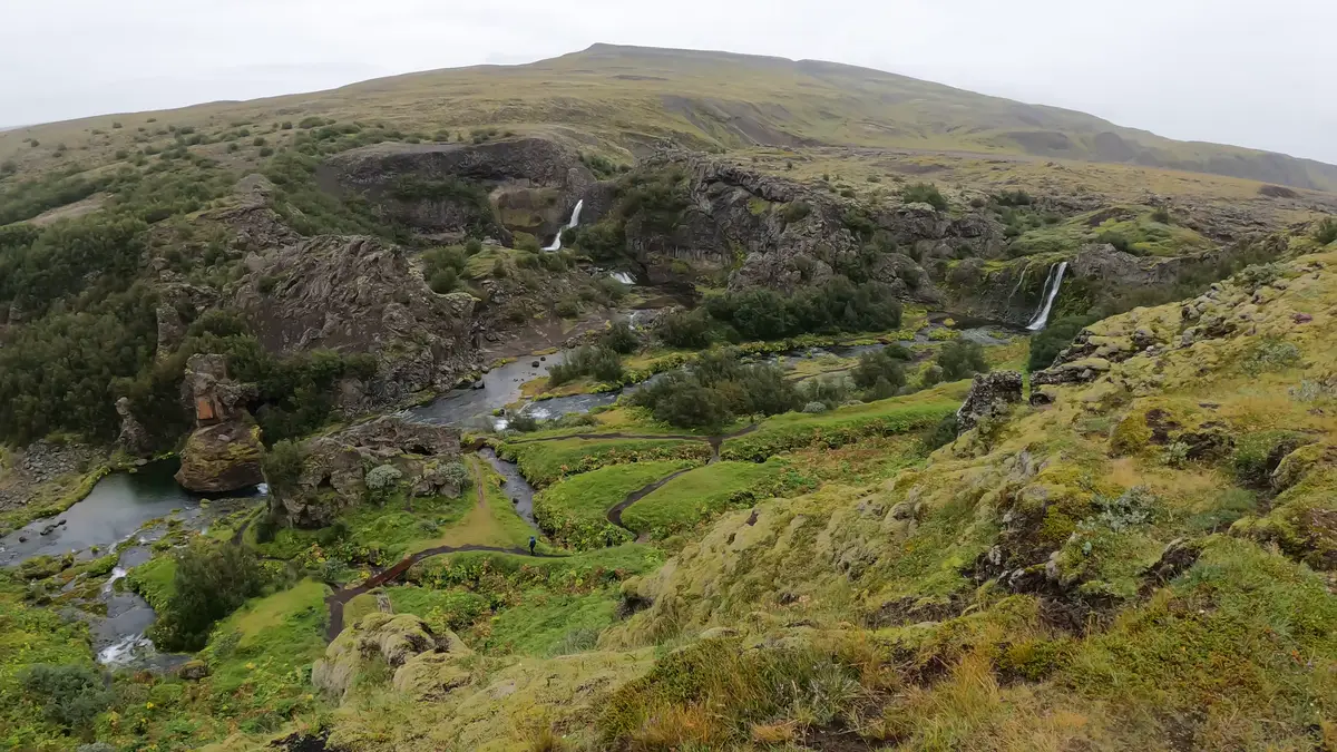 Vue panoramique de la vallée de Gjáin en Islande, avec cascades, rivières et sentiers serpentant à travers la végétation. Un joyau caché idéal à explorer en camping-car.