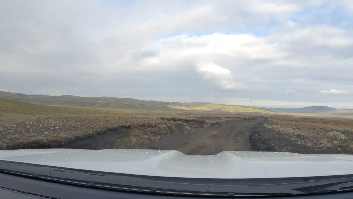 Vue depuis le pare-brise d’un camping-car roulant sur une piste en gravier dans les Hautes Terres d’Islande. Ces routes exigent un véhicule 4x4 pour explorer ces paysages sauvages en toute sécurité.