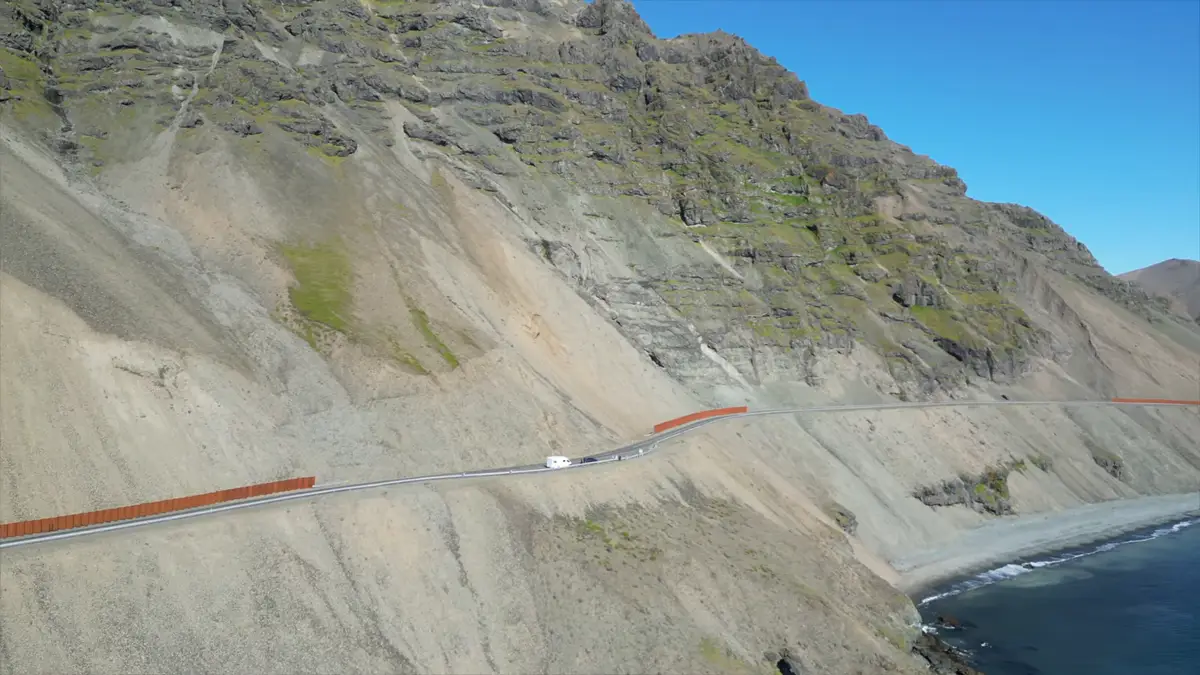 Camping-car parcourant une route panoramique le long d'une falaise en Islande, avec vue sur l'océan et des montagnes escarpées. Voyager en camping-car permet de découvrir des paysages impressionnants loin des routes conventionnelles.