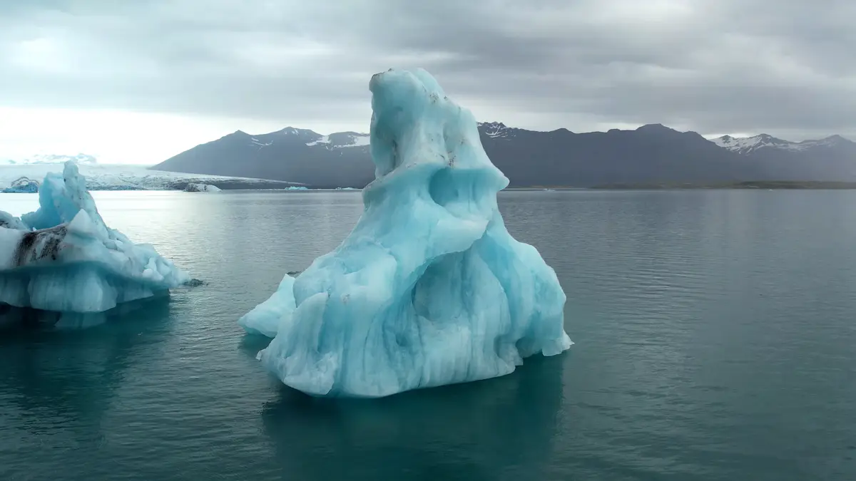 Un majestueux iceberg flottant sur la lagune glaciaire Jökulsárlón en Islande, avec des montagnes enneigées en arrière-plan. Une étape incontournable d’un road trip en camping-car.