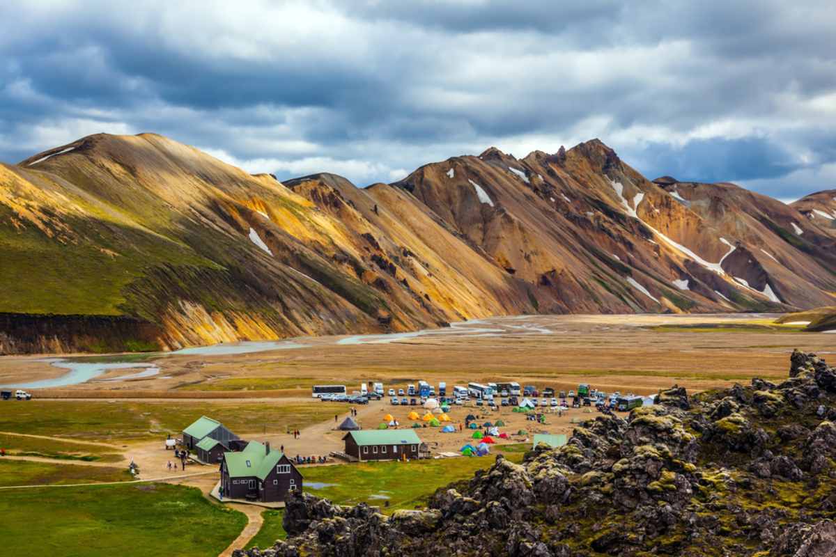 Camping en Islande : équipements essentiels Vue sur une cascade depuis l’arrière d’un camping-car avec ses propriétaires allongés sur le lit
