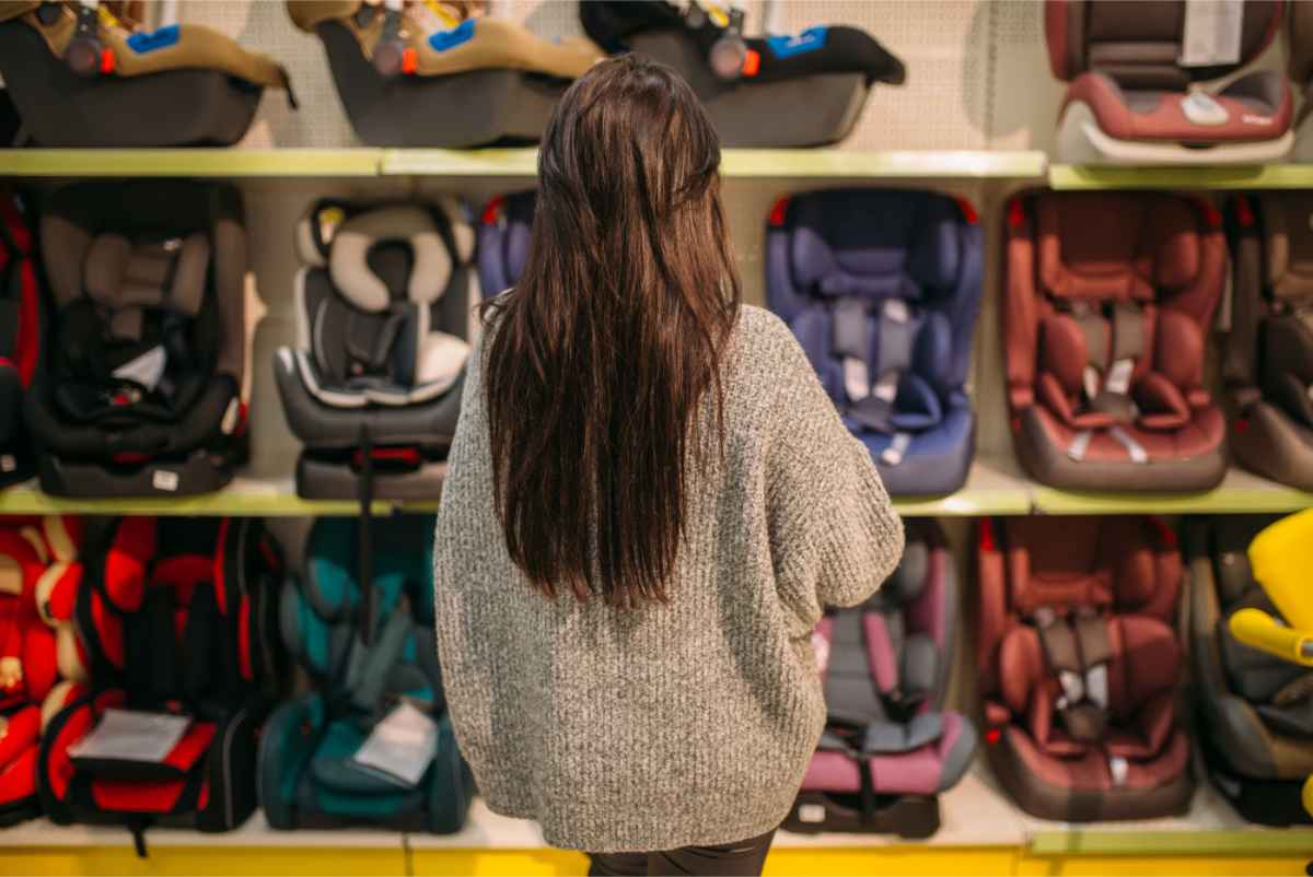 Femme devant plusieurs si&egrave;ges auto pour enfants dans un magasin