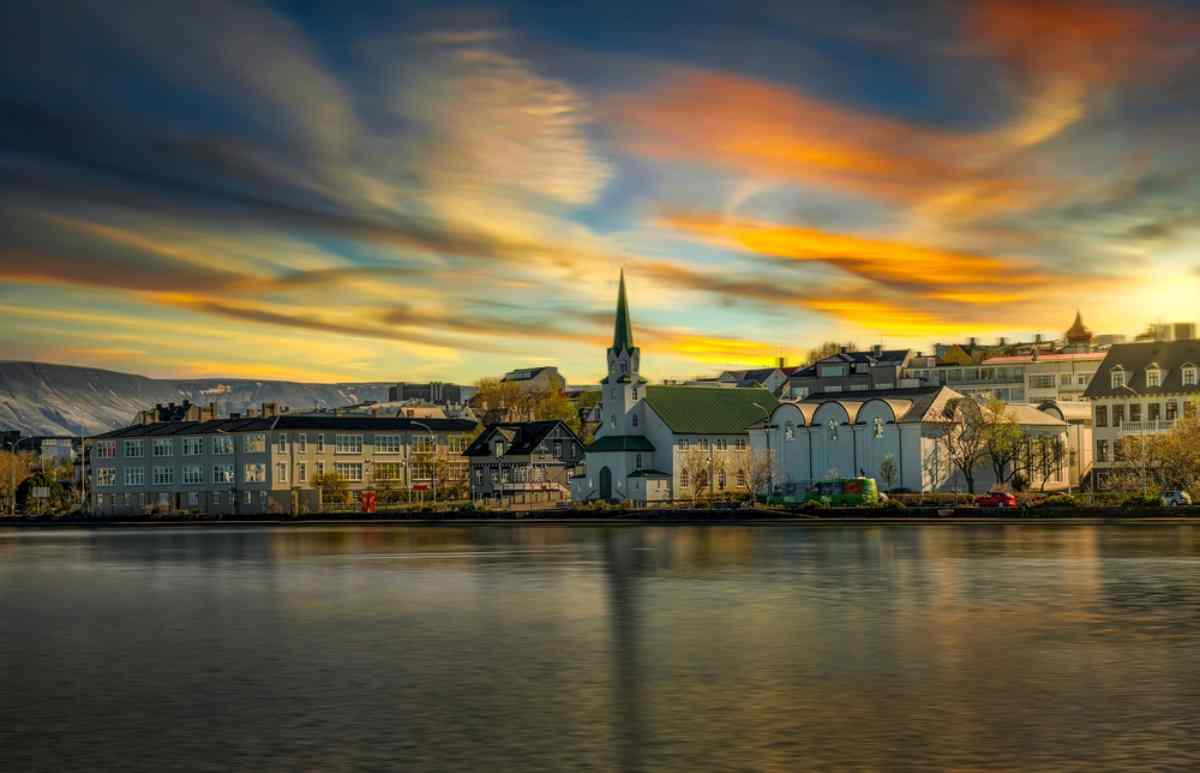 Vue de la baie de Reykjavik par une journée nuageuse où l’on peut voir certaines tours des bâtiments de la ville et leur reflet dans l’eau.