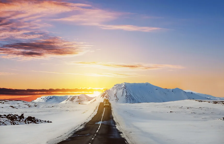 Vue générale d'une route goudronnée islandaise lors d'un coucher de soleil hivernal et d'une chute de neige complète.
