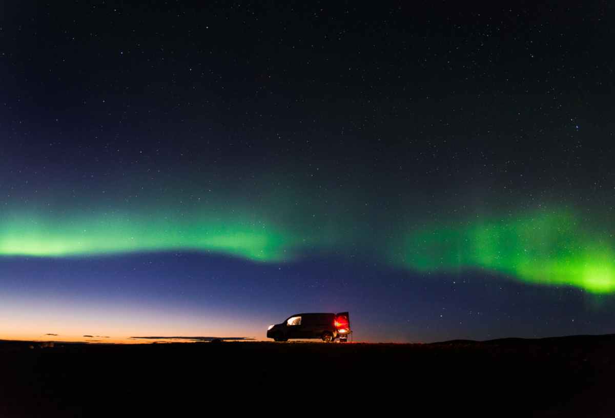 Aurores boréales dansant au-dessus d’un camping-car de location blanc en Islande