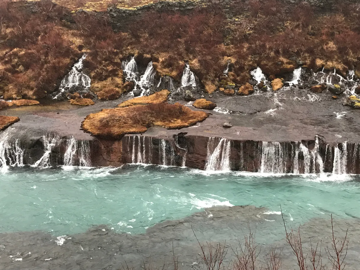 Vue d'ensemble d'une douce cascade islandaise pendant ce qui semble être les derniers vestiges de l'automne en raison de la couleur de la végétation.