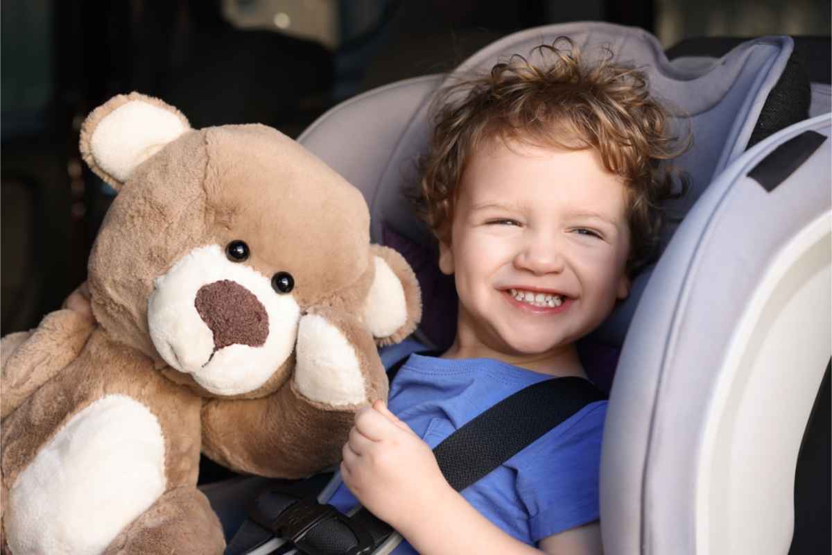 Enfant heureux assis dans son siège auto avec un ours en peluche à ses côtés